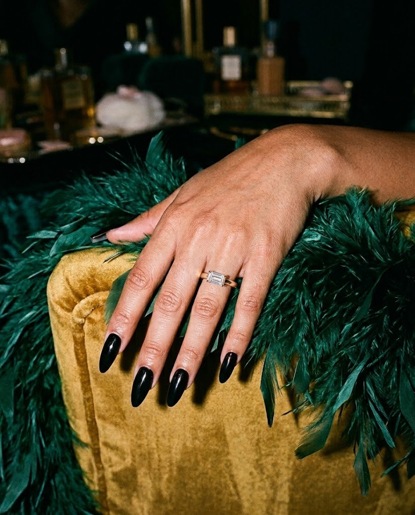 Celina east-west emerald cut ring on a hand resting on an emerald feather boa