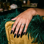 Celina east-west emerald cut ring on a hand resting on an emerald feather boa