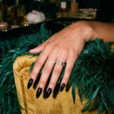 Celina east-west emerald cut ring on a hand resting on an emerald feather boa