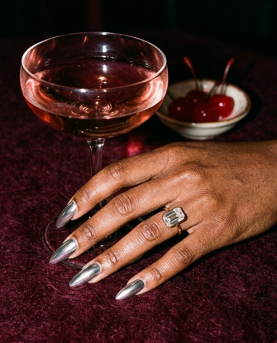 Esme ring on a hand beside a coupe glass at a night-time bar