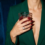 Esme ring on a hand holding a crystal tumbler, emerald suit, night-time