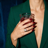 Esme ring on a hand holding a crystal tumbler, emerald suit, night-time